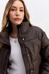 Campera puffer de corte cropped, color marrón oscuro, con cuello alto, cierre frontal con cremallera y botones a presión, y puños elásticos.
