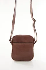 Morral bandolera de cuero genuino color marrón, con diseño compacto, cierre superior y correa ajustable para el hombro.