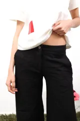 Pantalón amplio de lino blanco, tiro medio/bajo, con bolsillos delanteros y trasero, y botón metálico grabado. Presenta bordados laterales y traseros.