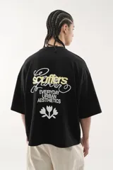 Remera negra de algodón con corte oversize y cuello redondo acanalado. Presenta un estampado grande en la espalda con texto en blanco y amarillo que incluye la palabra "Scuffers", "Garden", "Everyday Urban Aesthetics" y un diseño de flores blancas.