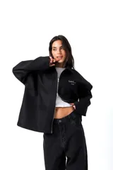 Camisa de gabardina negra de diseño unisex y corte holgado. Cuenta con un cierre frontal de doble camino, cuello camisero y detalles de estampa y bordado en el pecho con el texto 'Low Profile'.