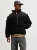 Campera puffer con cuello alto y cierre frontal, confeccionada en tejido teddy negro con paneles superiores lisos. Cuenta con bolsillos laterales y relleno de poliéster.