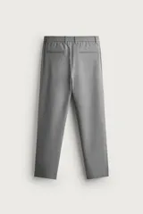 Pantalón de corte slim fit y color negro, confeccionado en tejido elástico. Cuenta con cintura elástica, trabillas, bolsillos frontales y cierre con cremallera y botón.