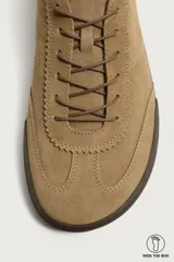 Zapatilla deportiva barefoot de hombre, confeccionada en piel con acabado serraje de color marrón, puntera redondeada, suela fina de goma oscura y detalles en cuero liso en el talón.