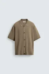 Camisa de punto de manga corta, color marrón topo, con cuello solapa y cierre frontal de botones. Presenta un tejido texturizado y un calce relajado.