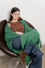 Poncho tejido color verde con cuello alto y flecos largos.