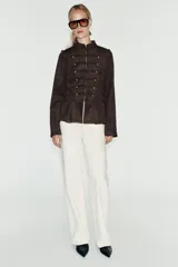 Chaqueta de gamuza marrón con cuello alto, manga larga y bajo con peplum. Cuenta con doble botonadura decorativa de botones metálicos dorados en el frente y cierre con ganchos ocultos.