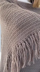 Poncho tejido en lana merino color marrón, con diseño de punto acanalado y terminación con flecos en el borde inferior. Incluye una pequeña etiqueta de cuero en la parte posterior.