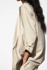 Blazer color beige confeccionada en lino, de corte recto, con cuello solapa, hombreras y mangas 3/4 con trabilla y botón dorado.