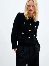 Chaqueta de estilo tweed en color negro, con cuello redondo, cierre frontal de botones dorados y bolsillos delanteros con solapa. Presenta un diseño de silueta recta y acabado deshilachado en los bordes.