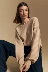 Sweater color crema con mangas abullonadas y puños elastizados. Presenta una textura tejida en relieve con patrón de ladrillos en el cuerpo y rayas horizontales en las mangas.