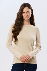 Buzo tejido de algodón color beige, de manga larga, con cuello redondo y delicados motivos bordados distribuidos en la prenda.