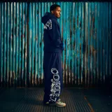 Pantalón de jogging azul marino con estampado gráfico blanco en la pierna derecha y logo circular en la pierna izquierda. Cuenta con cintura elástica y bolsillos laterales.