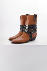 Bota de cuero color marrón con puntera fina y taco bajo. Presenta correas de cuero negro con apliques metálicos plateados.