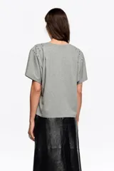 Camiseta de corte recto y escote redondo, con mangas cortas que presentan pliegues en los hombros y detalle de remaches metálicos decorativos.