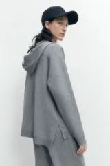 Sweater gris melange de tejido de punto, con capucha y cordones cruzados en el escote.
