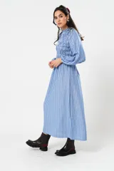 Vestido largo a rayas verticales azules y blancas, con manga globo y diseño de nido de abeja con hilo elástico hasta la cintura. Cuello alto fruncido y falda amplia con caída fluida.