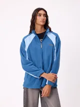 Campera de polar marca Rusty, color azul con paneles laterales en celeste claro. Presenta cierre frontal completo, cuello alto y logo de la marca bordado en el pecho.