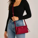 Cartera bandolera Guess modelo Devon de poliuretano color rojo con acabado texturizado brillante, herrajes dorados y el logo triangular de la marca en el centro. Cuenta con cierre superior y correa ajustable.