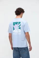 Remera celeste de manga corta con calce relaxed, confeccionada en jersey de algodón pesado con textura suave. Presenta un diseño estampado en la espalda que incluye un paisaje de montaña con un sol y la inscripción 'WILD PEAK'.