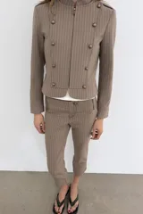 Pantalón capri de tiro medio con raya diplomática en tonos beige y marrón. Presenta trabillas, bolsillos laterales y cierre frontal con cremallera y botón metálico.