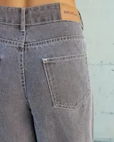 Pantalón de jean color beige, de corte recto y tiro alto, con ruedo deshilachado y cierre frontal con botón y cremallera.