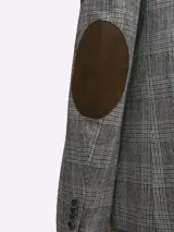 Saco de paño marrón con diseño a cuadros en tonos marrón, rojo y blanco. Tiene cuello con solapas, bolsillos de plastrón en pecho y cadera, mangas con coderas en contraste de color, forro estampado y aberturas en espalda.