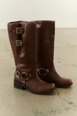 Bota de cuero marrón de caña alta con herrajes plateados, taco bajo y punta redondeada.