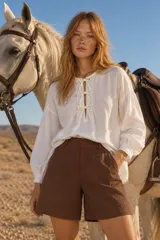 Blusa blanca de manga larga con cuello alto y volados, cierre frontal con lazos y diseño holgado.