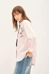 Camisa de algodón color rosado con cuello mao, cierre frontal con botones de nácar y bordado artesanal multicolor en el pecho. Presenta un cordón decorativo en el cuello con borlas.