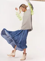 Buzo tejido oversized con bloques de color blanco y gris, cuello redondo en verde neón, tajos laterales y flecos verdes en las mangas.