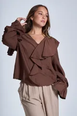 Blusa de color marrón con escote en V, mangas largas abullonadas con puños elásticos y detalles de volados en los hombros y el frente.