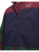 Campera deportiva Under Armour modelo Icon Woven Track FZ, con diseño colorblock en tonos bordó, azul marino y verde. Cuenta con cierre frontal completo, cuello alto y bolsillos laterales.