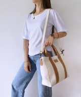 Bolso tipo tote de lona color crudo con detalles en cuero color marrón. Tiene doble asa corta de mano y correa larga de hombro.