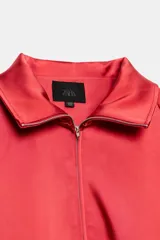 Cazadora roja de satén con cuello subido, manga larga con hombreras, bolsillos delanteros con cierre, bajo ajustable con cordón elástico y cierre frontal de cremallera metálica.