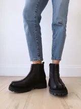 Botas negras de cuero con caña baja, cierre lateral con cremallera y suela track.