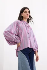 Camisa holgada de popelina de algodón con rayas verticales en tonos rosado, gris y blanco. Presenta cuello alto con volado, hombros caídos, mangas anchas abullonadas y cierre frontal con botones.