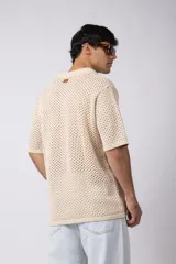 Camisa de punto calado en color beige, de manga corta y corte relajado. Presenta cuello tipo bowling, cierre frontal con botones al tono y una estructura liviana y respirable confeccionada en algodón.