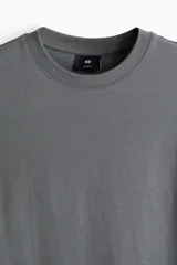 Remera de algodón de peso medio color gris, con cuello redondo ribeteado, hombros caídos, mangas cortas y corte relajado.