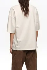 Remera oversize color blanco crudo, confeccionada en algodón, con cuello redondo y mangas cortas. Presenta un estampado frontal en color rojo de un jarrón con flores y el logo de la marca en caligrafía.