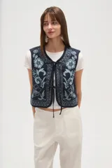 Chaleco sin mangas, color azul marino, con bordados florales en tono celeste claro. Presenta un escote en V y se cierra al frente con lazos ajustables.
