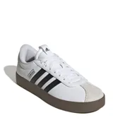 Championes Adidas modelo VL Court 3.0, de diseño urbano inspirado en el skate. Presentan una parte superior de cuero sintético blanco con las icónicas tres tiras laterales en negro y puntera de gamuza en tono gris claro. Cuentan con suela vulcanizada de color marrón y cierre mediante cordones.