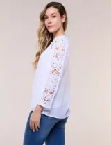 Blusa blanca de gasa liviana con forro interno en el cuerpo, de estilo boho-chic y silueta semi holgada. Presenta escote redondo con canesú de encaje calado en el frente y mangas largas con paneles longitudinales de encaje.
