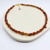 Collar tipo gargantilla elaborado con escallas de ámbar natural en tonos rojizos y marrones, con cierre y detalles metálicos con baño de oro.