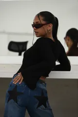 Jean de mezclilla azul de corte recto y tiro medio, con un gran parche negro en forma de estrella en el bolsillo trasero.