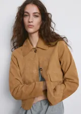 Chaqueta corta de piel caprina en color tostado, con cuello camisero, cierre frontal de botones y bolsillos de parche con solapa en el pecho.