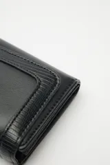 Billetera compacta de cuero sintético negro, con solapa que combina texturas lisas y efecto reptil. Incluye un aplique metálico circular con logo grabado en el frente y cierre con broche.
