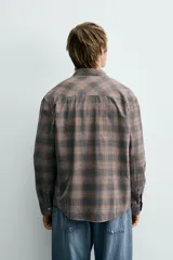 Camisa de corte relajado confeccionada en algodón, con estampado de cuadros en tonos marrones y grises. Presenta cuello abotonado, cierre frontal de botones y mangas largas con puños abotonados.