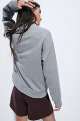 Buzo de corte relajado con cuello redondo y hombros caídos. Presenta un estampado frontal con letras estilizadas y ribetes acanalados en cuello, puños y bajo.