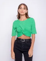 Top corto verde con textura, escote redondo y mangas cortas. Presenta un nudo en la parte delantera.